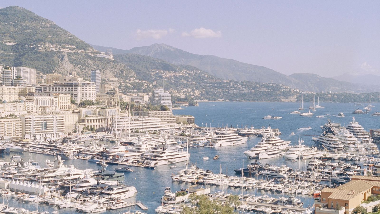 Port Hercule in Monaco filled with luxury yachts, with Monte Carlo and the Riviera coastline behind