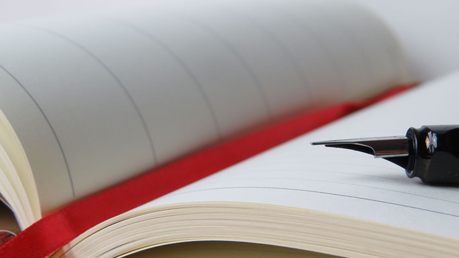 Fountain pen resting on an open notebook with a red ribbon bookmark, evoking contract signing