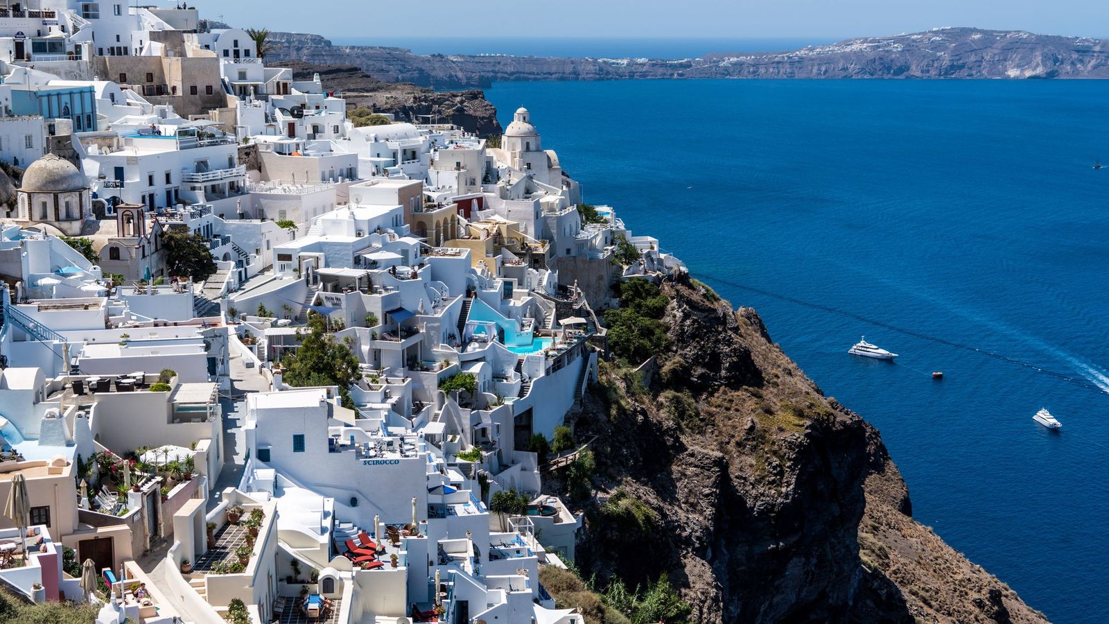 Whitewashed cliffside hotels with terraces and pools overlooking the Santorini caldera
