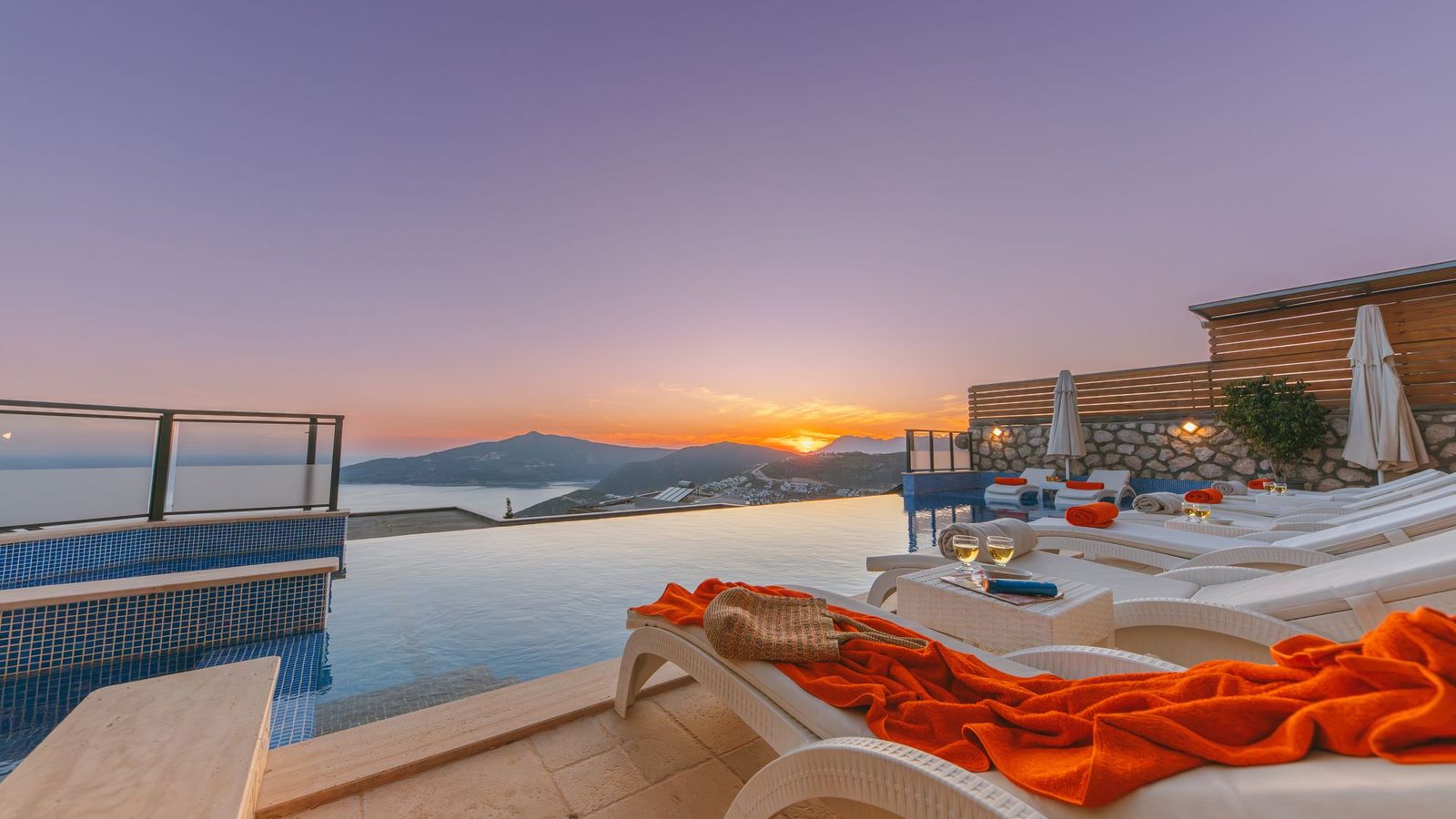 Luxury villa infinity pool with sun loungers overlooking the Mediterranean sea and hills at sunset